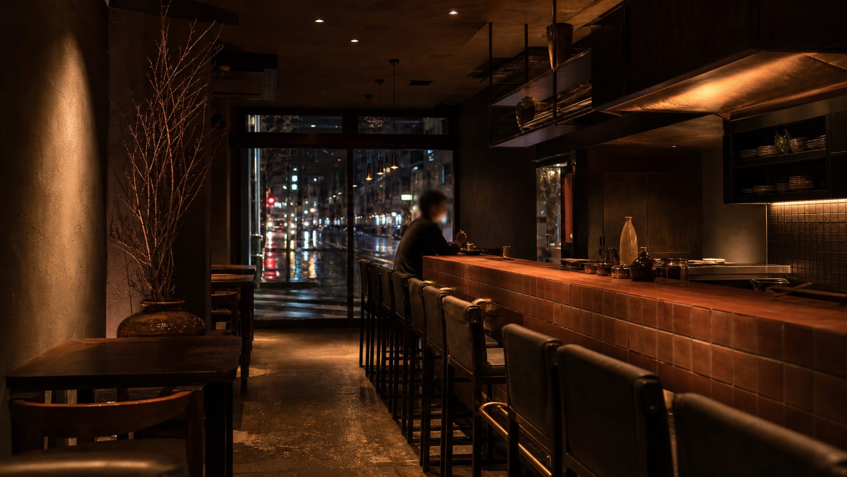 The counter on handover night. Terracotta tile, a brass footrail, and the street lit up beyond the glass